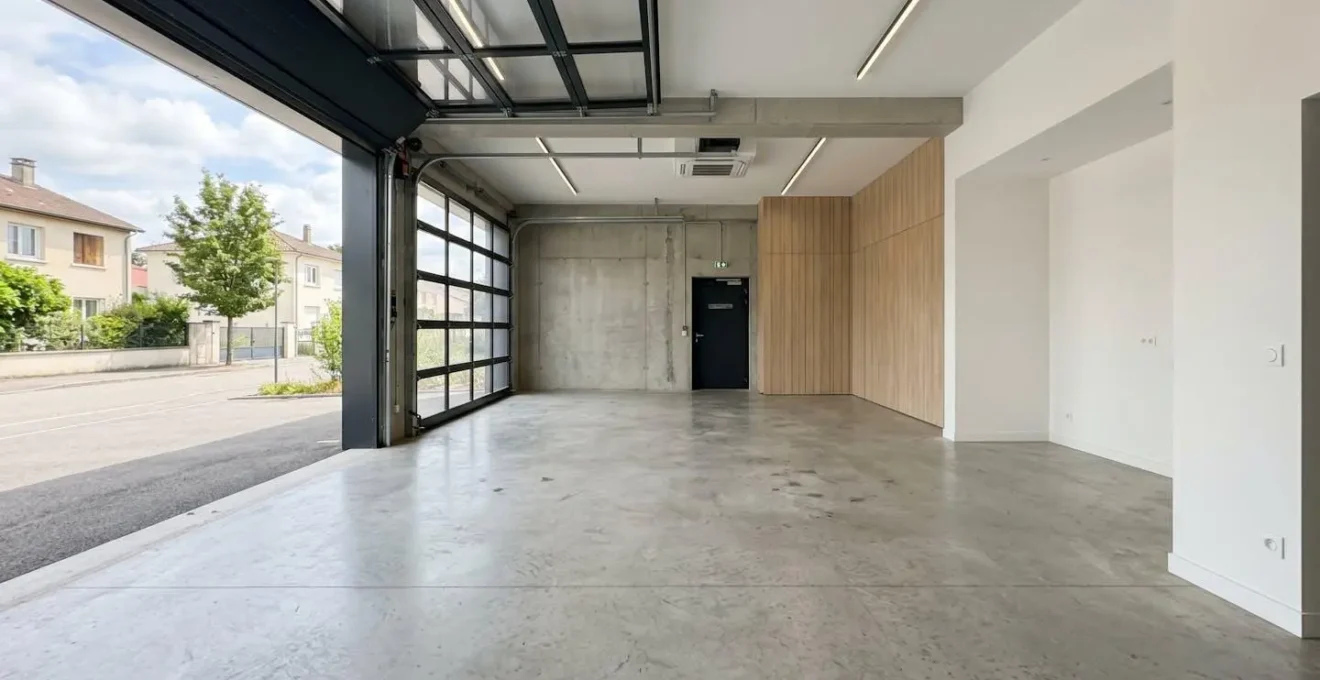 Vue en angle large d'un garage moderne vide avec sol en dalle béton lisse et lumière naturelle entrant par la porte